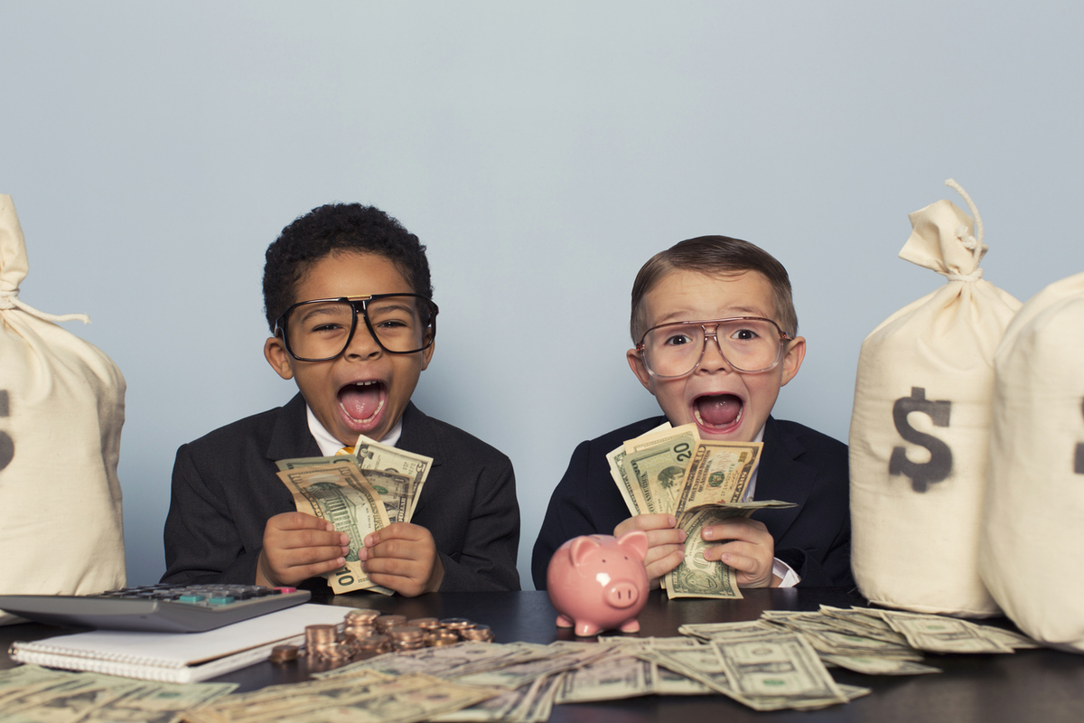 Two kids holding money with money on the table in front of them